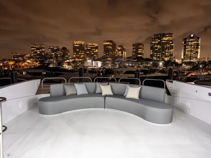 Luxury yacht deck at night with city skyline and curved sofa.