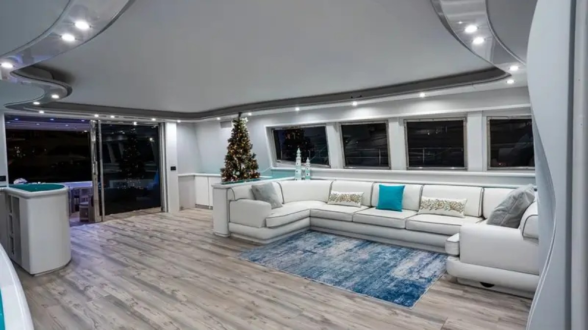 Modern yacht interior with white sectional sofa, Christmas tree, and blue accents.