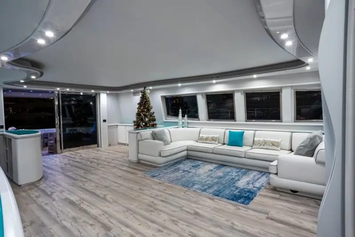 Modern yacht interior with white sectional sofa, Christmas tree, and blue accents.