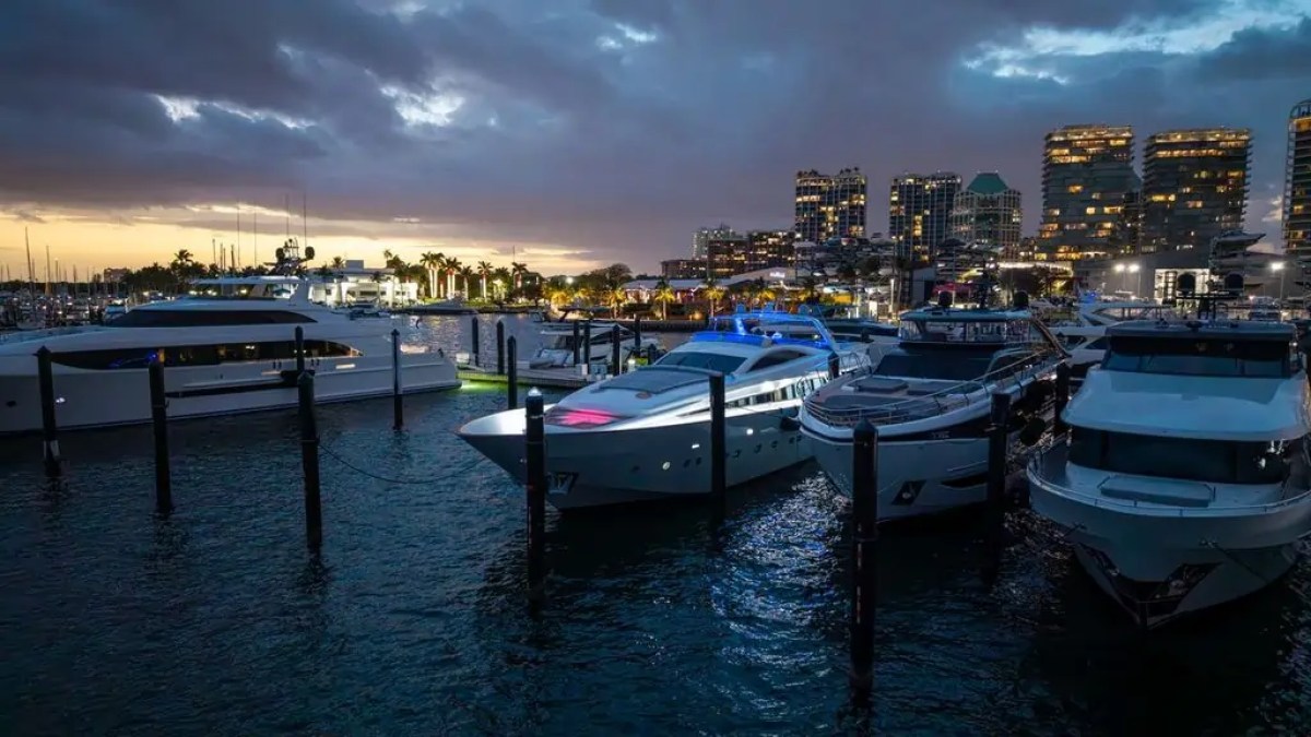 Yachts docked at a marina during twilight with city skyline in the background.