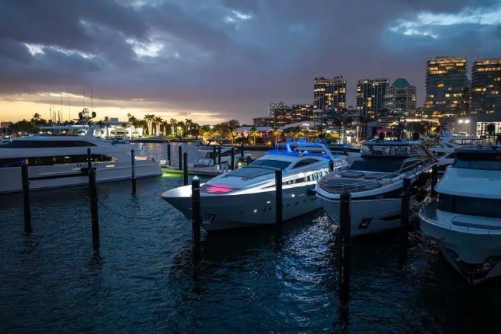 Yachts docked at a marina during twilight with city skyline in the background.