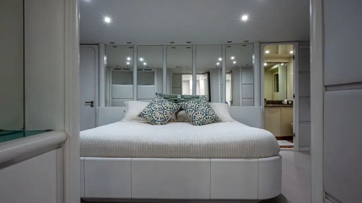 Modern bedroom with a large white bed, mirrored closet doors, and decorative pillows.