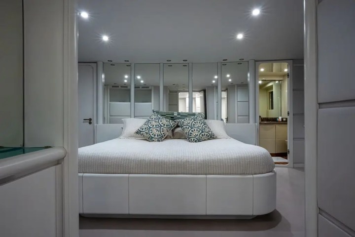 Modern bedroom with a large white bed, mirrored closet doors, and decorative pillows.