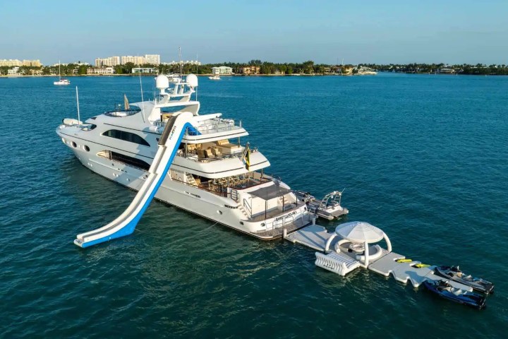 Luxury yacht with waterslide and inflatable dock on a sunny bay.