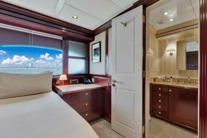 Room with a bed, wood cabinets, and a bathroom, window view of sea and clouds.