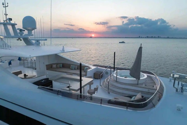 Luxury yacht deck with jacuzzi, seating, and sunset over calm ocean.