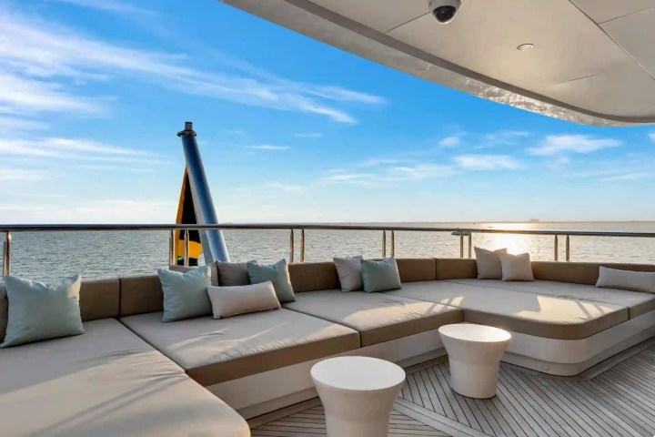 Spacious yacht deck with cushioned seating and tables, overlooking calm ocean waters at sunset.