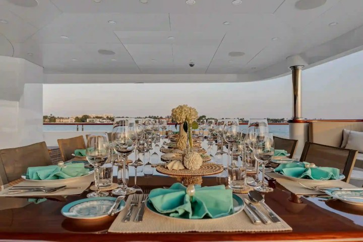 Elegant outdoor dining setup on a yacht with turquoise napkins and flowers.