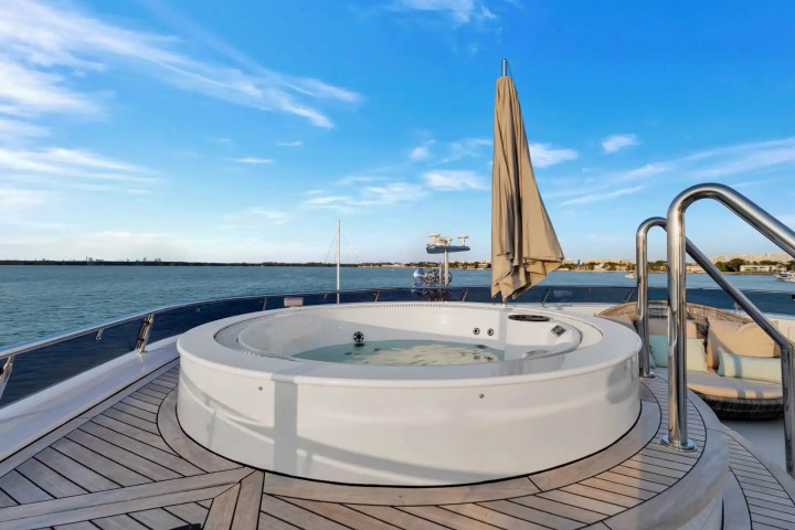 Deck of a yacht with a hot tub and umbrella, overlooking calm sea and blue sky.