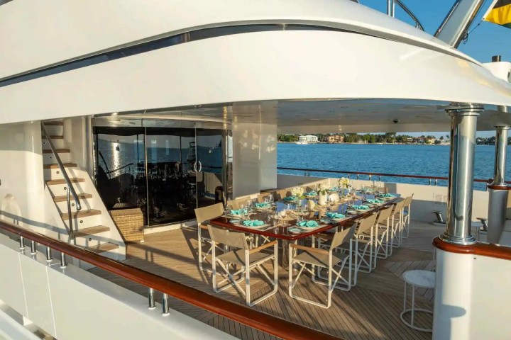 Luxury yacht deck with dining table set for twelve, overlooking a calm sea and distant shore.