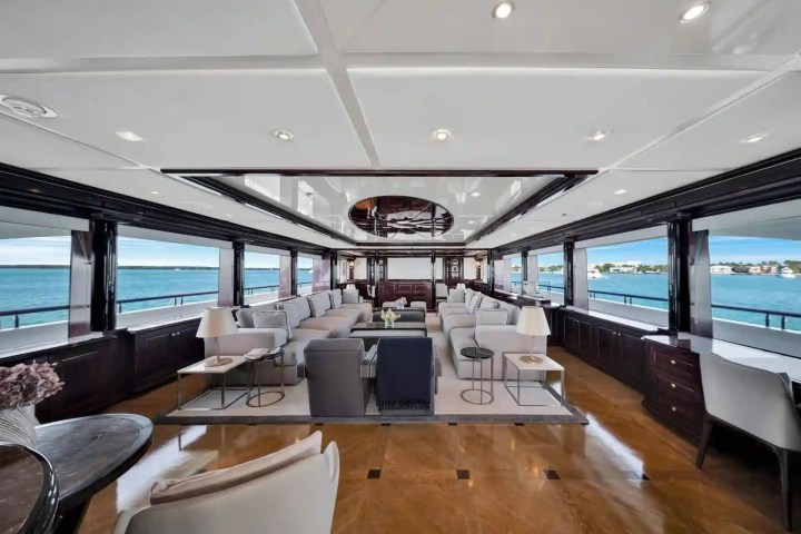 Luxurious yacht interior with sofas, wooden flooring, and ocean views through large windows.