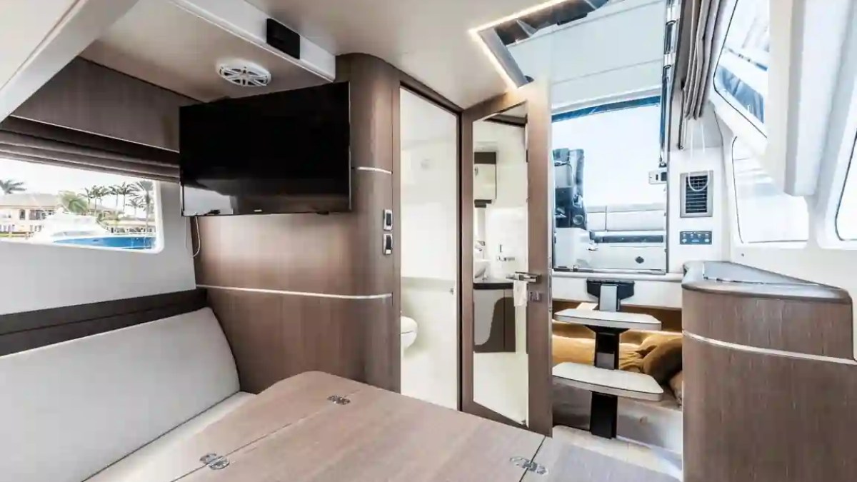 Interior of a yacht with a table, TV, and open door leading outside to seating area.