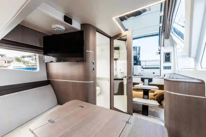 Interior of a yacht with a table, TV, and open door leading outside to seating area.