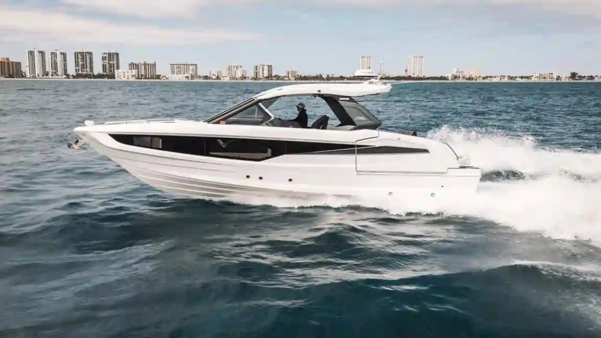 White speedboat cruising on blue ocean near city skyline under cloudy sky.