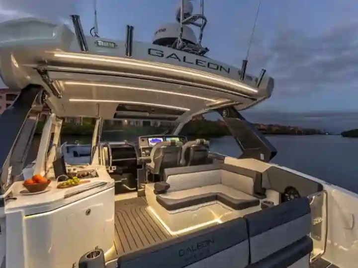 Modern yacht deck with seating, table, and night lighting overlooking calm water at dusk.