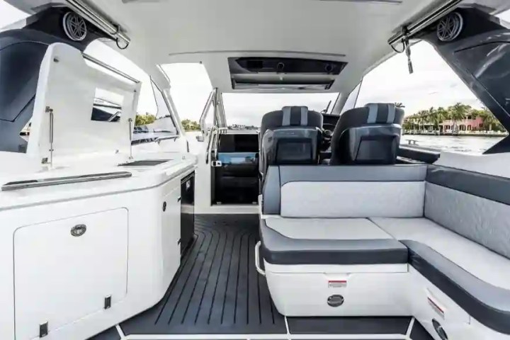 Interior of a modern boat with seats, open-air design, and a small kitchenette.