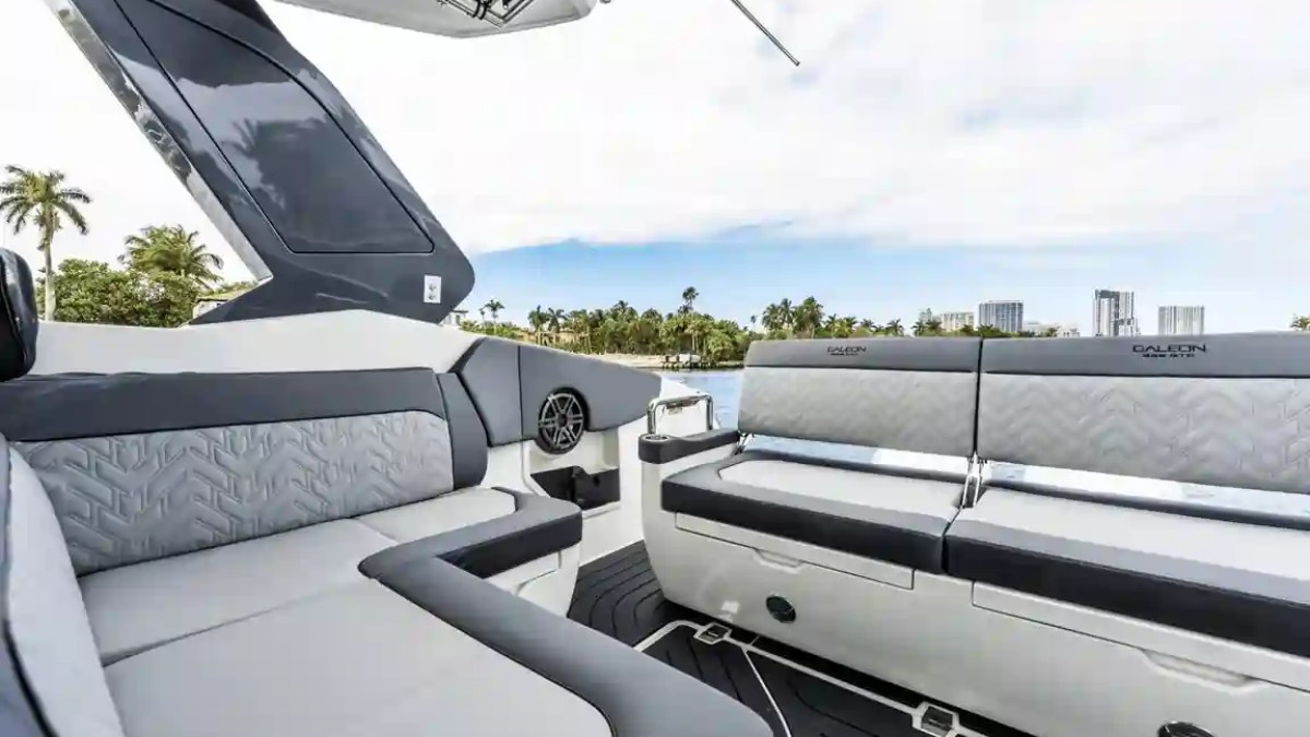 Modern boat interior with gray seating and palm trees visible through windows.