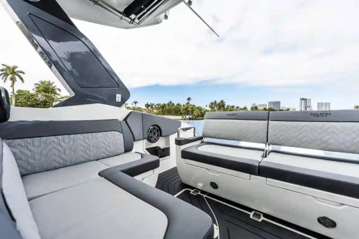 Modern boat interior with gray seating and palm trees visible through windows.