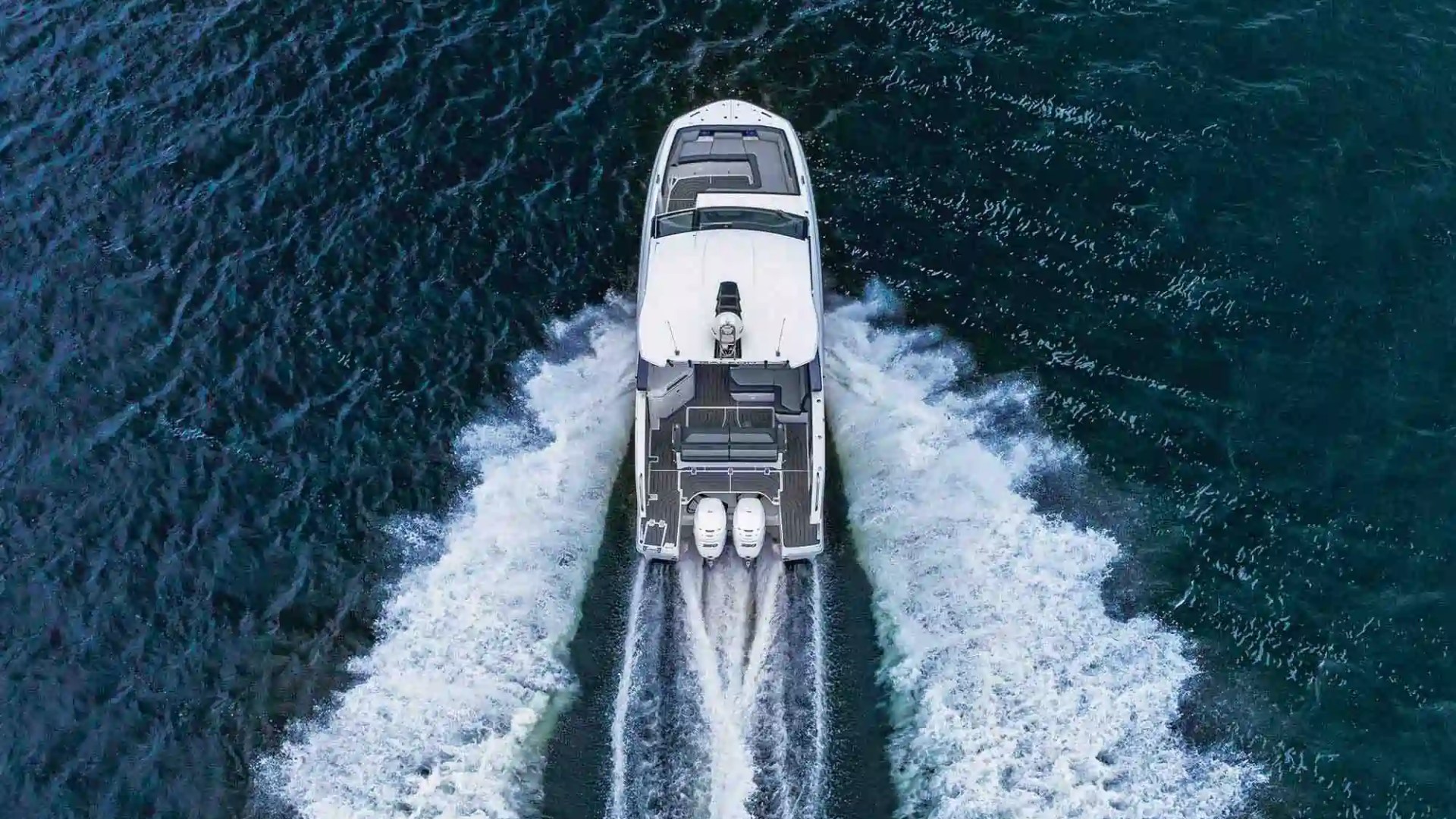 Overhead view of a white yacht speeding through blue water, leaving a wake behind.