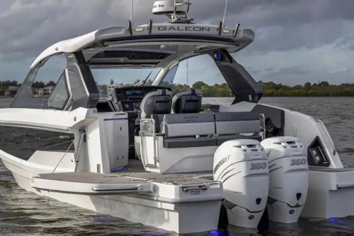Luxury boat with dual engines and seating, cruising on a cloudy day.