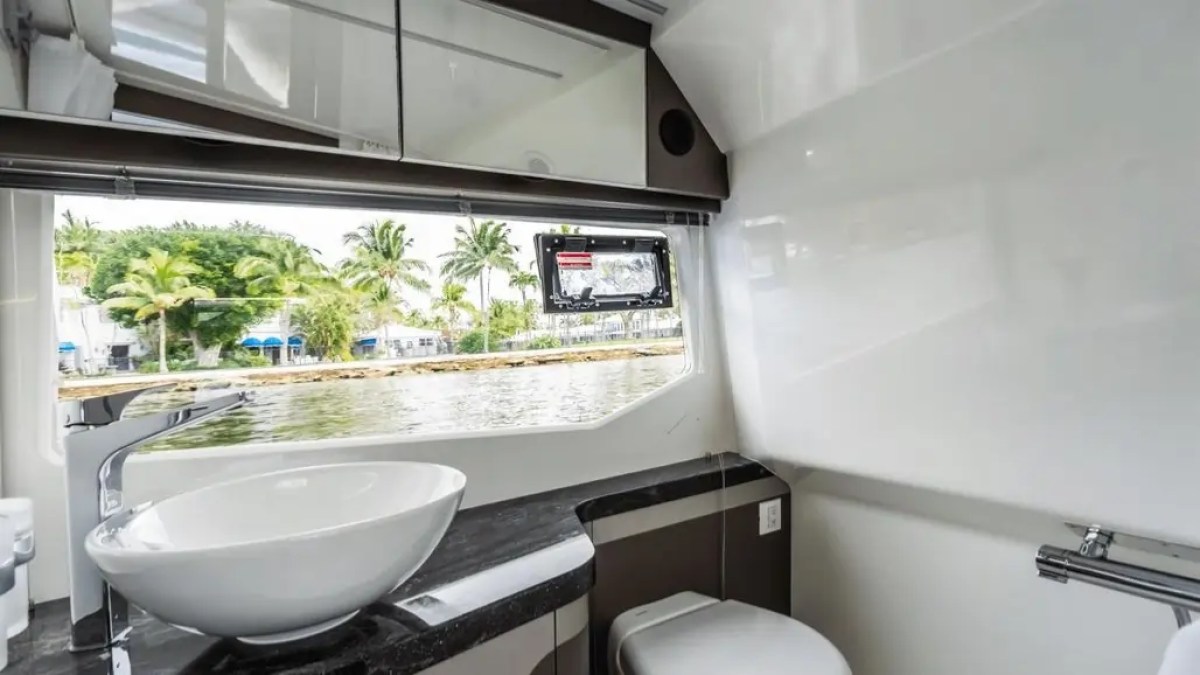 Boat bathroom with round sink, mirror, and window view of water and palm trees.
