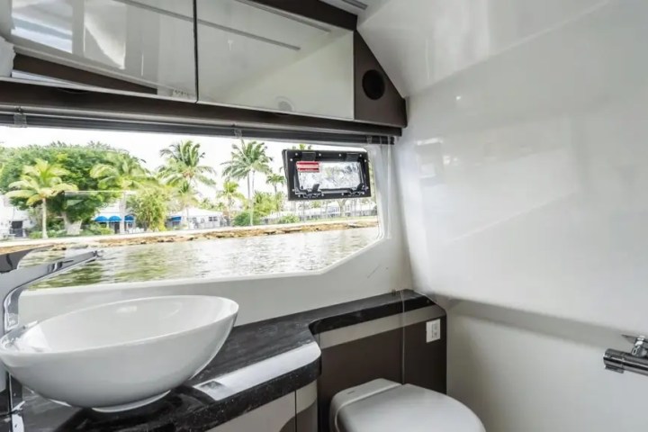 Boat bathroom with round sink, mirror, and window view of water and palm trees.
