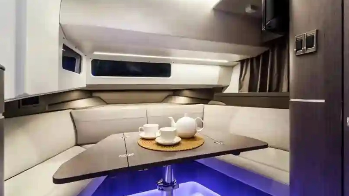 Interior of a boat cabin with a table, teapot, and cups on a mat, surrounded by cushioned seating.