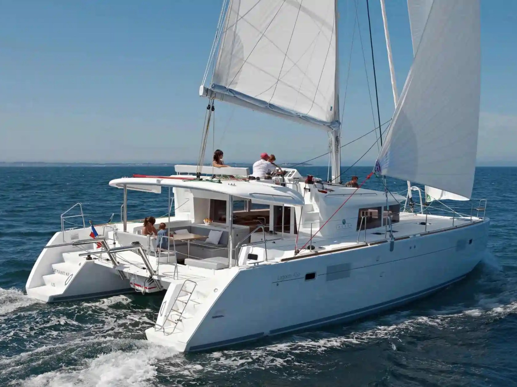 White catamaran sailing on the ocean with people on deck under clear blue skies.