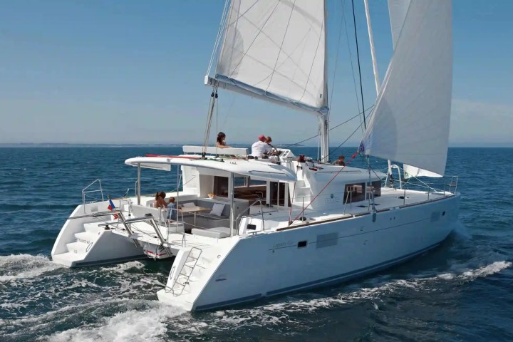 White catamaran sailing on the ocean with people on deck under clear blue skies.