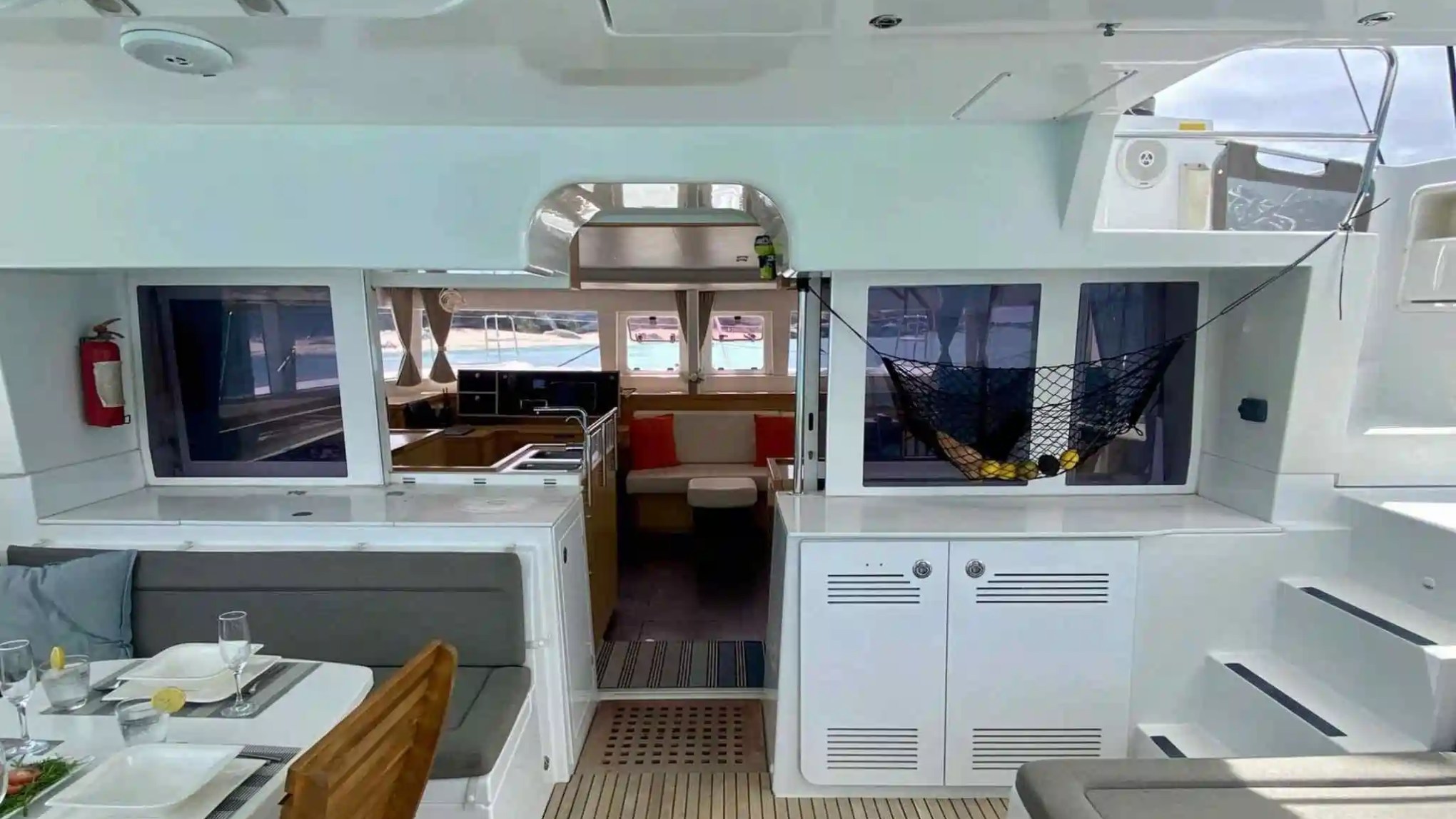 Interior of a yacht with dining area, kitchen, and net holding fruits.
