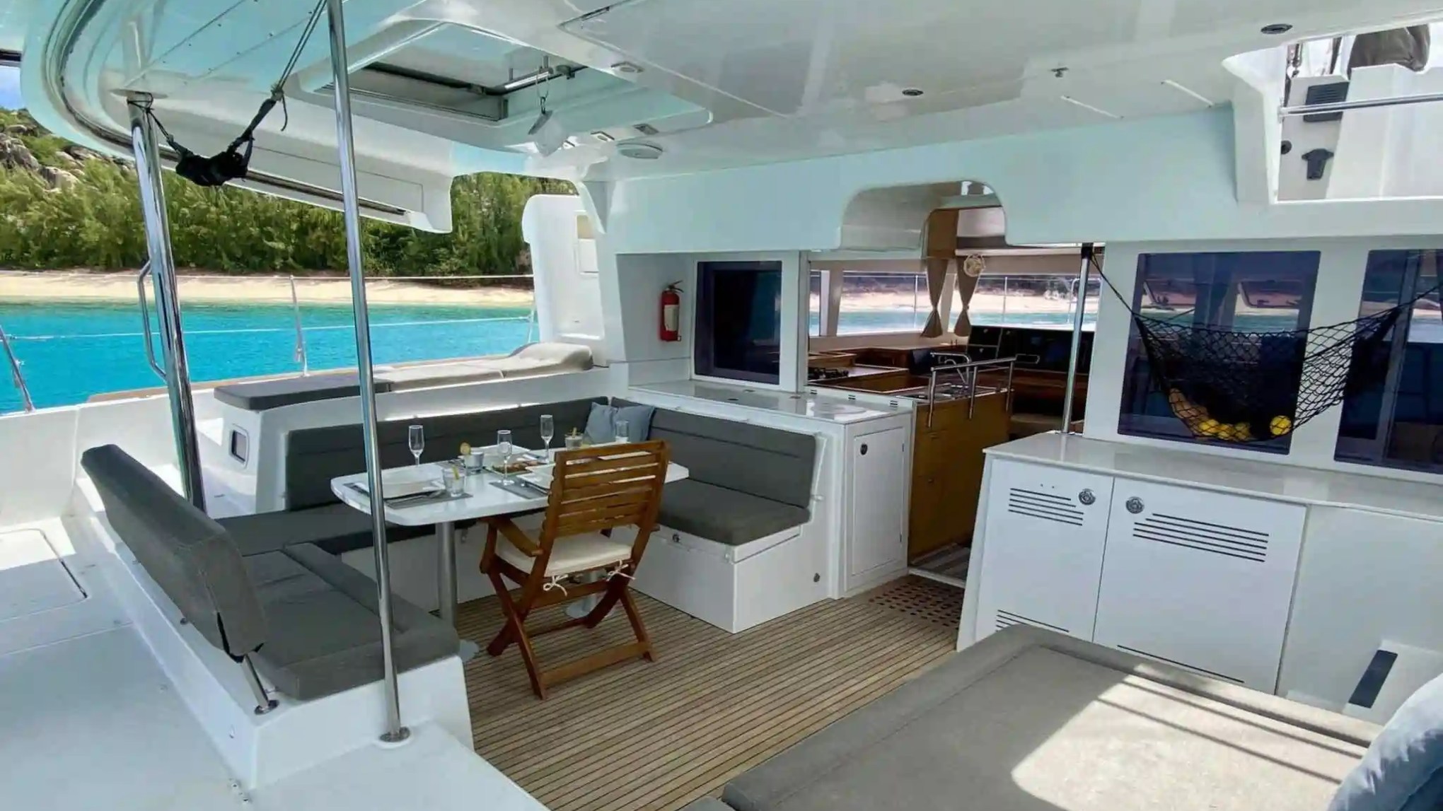 Interior of a yacht with dining table, seating, and view of beach and ocean.