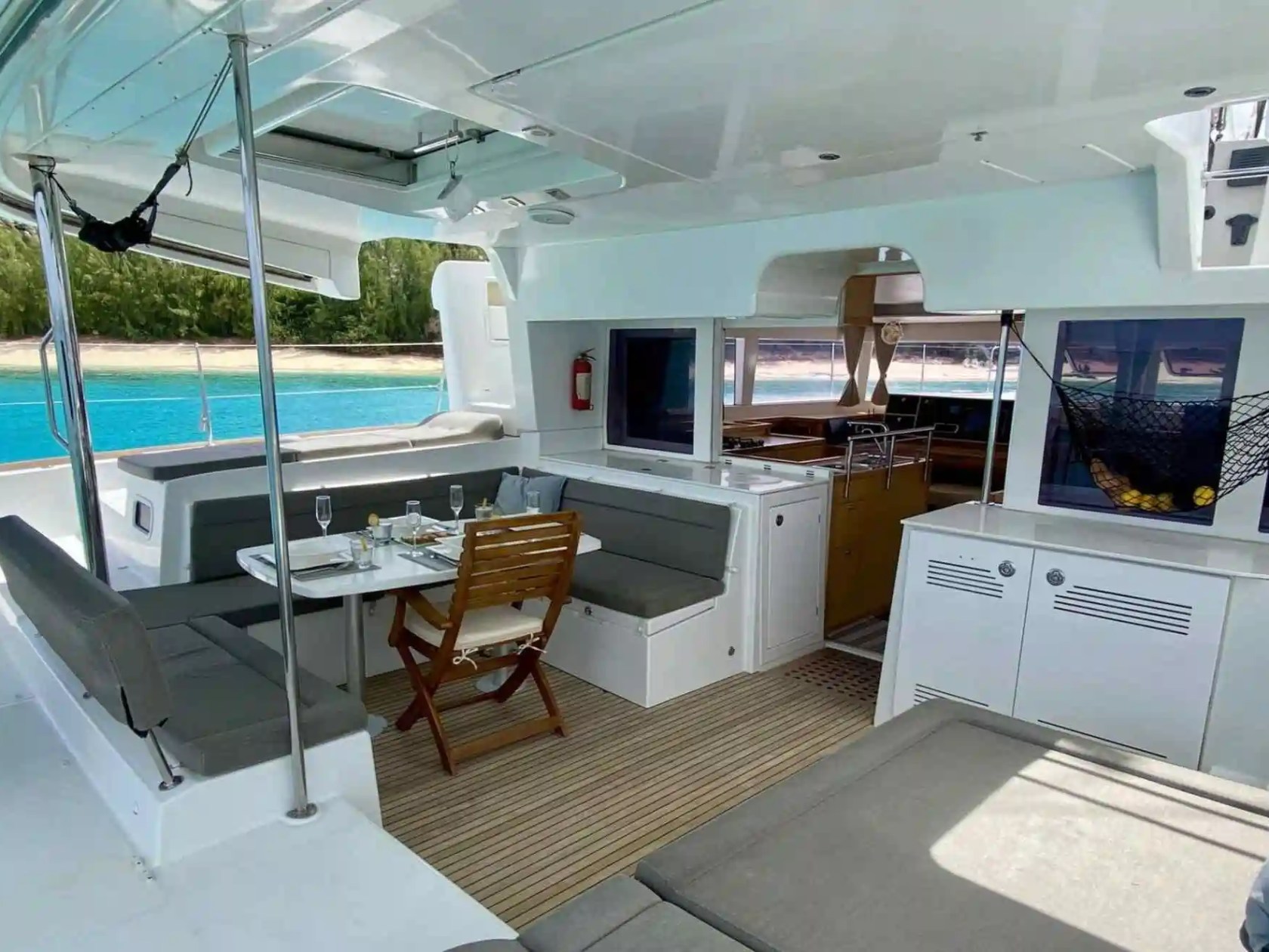 Interior of a yacht with dining table, seating, and view of beach and ocean.
