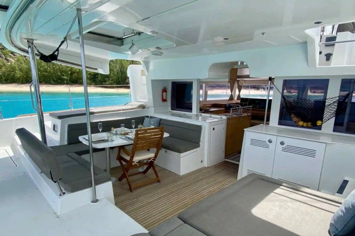 Interior of a yacht with dining table, seating, and view of beach and ocean.