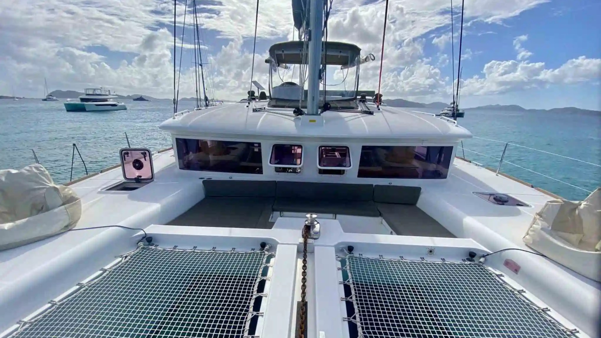 View from the deck of a catamaran sailboat on a sunny day, with ocean and other boats in the background.