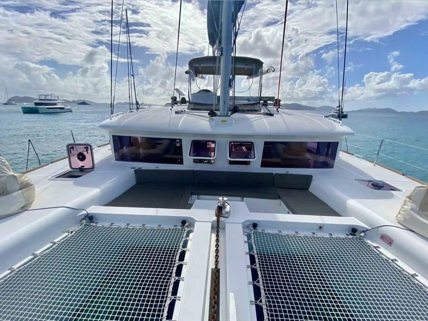 View from the deck of a catamaran sailboat on a sunny day, with ocean and other boats in the background.