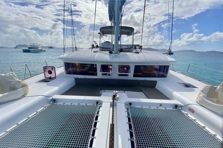 View from the deck of a catamaran sailboat on a sunny day, with ocean and other boats in the background.