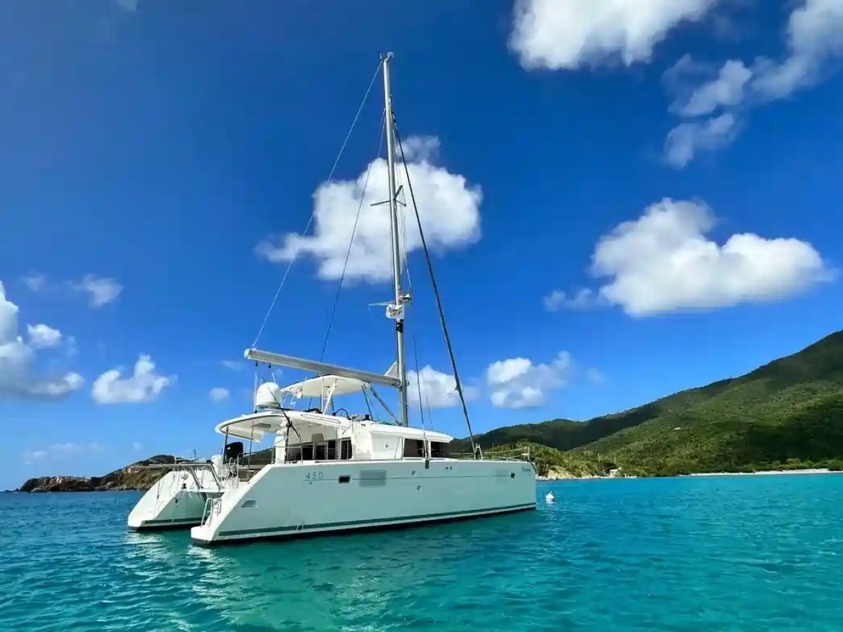 Sailboat on turquoise sea with cloudy sky and green hills in background.