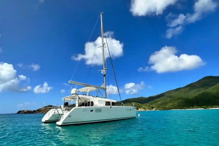 Sailboat on turquoise sea with cloudy sky and green hills in background.