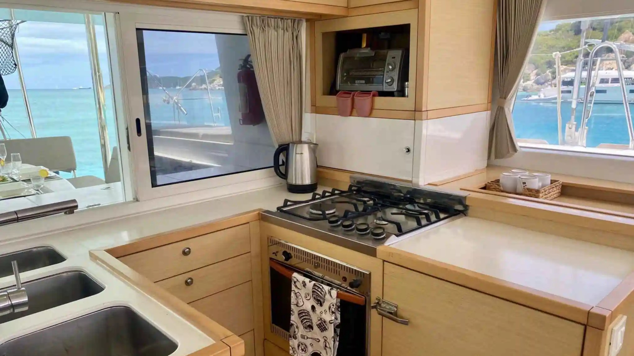 Boat kitchen with a stove, oven, sink, and window view of the sea.