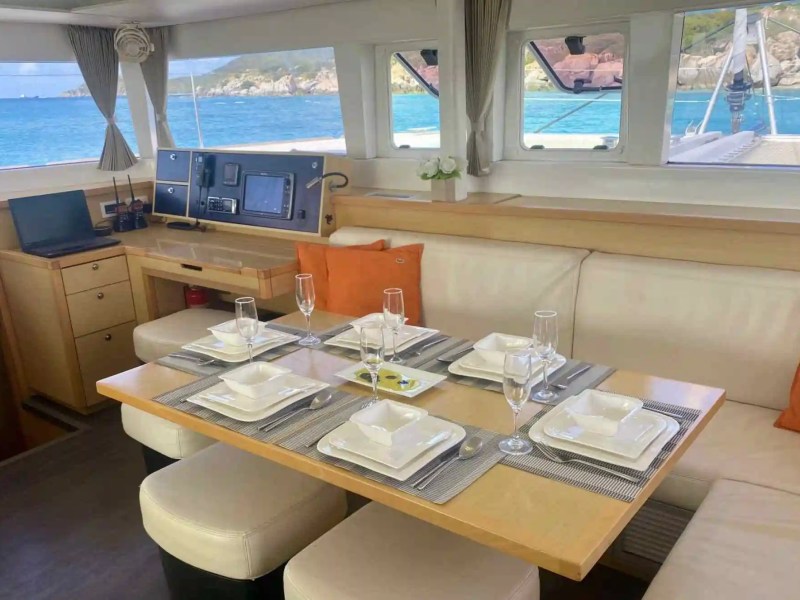 Interior of a yacht with a set dining table and ocean view through windows.