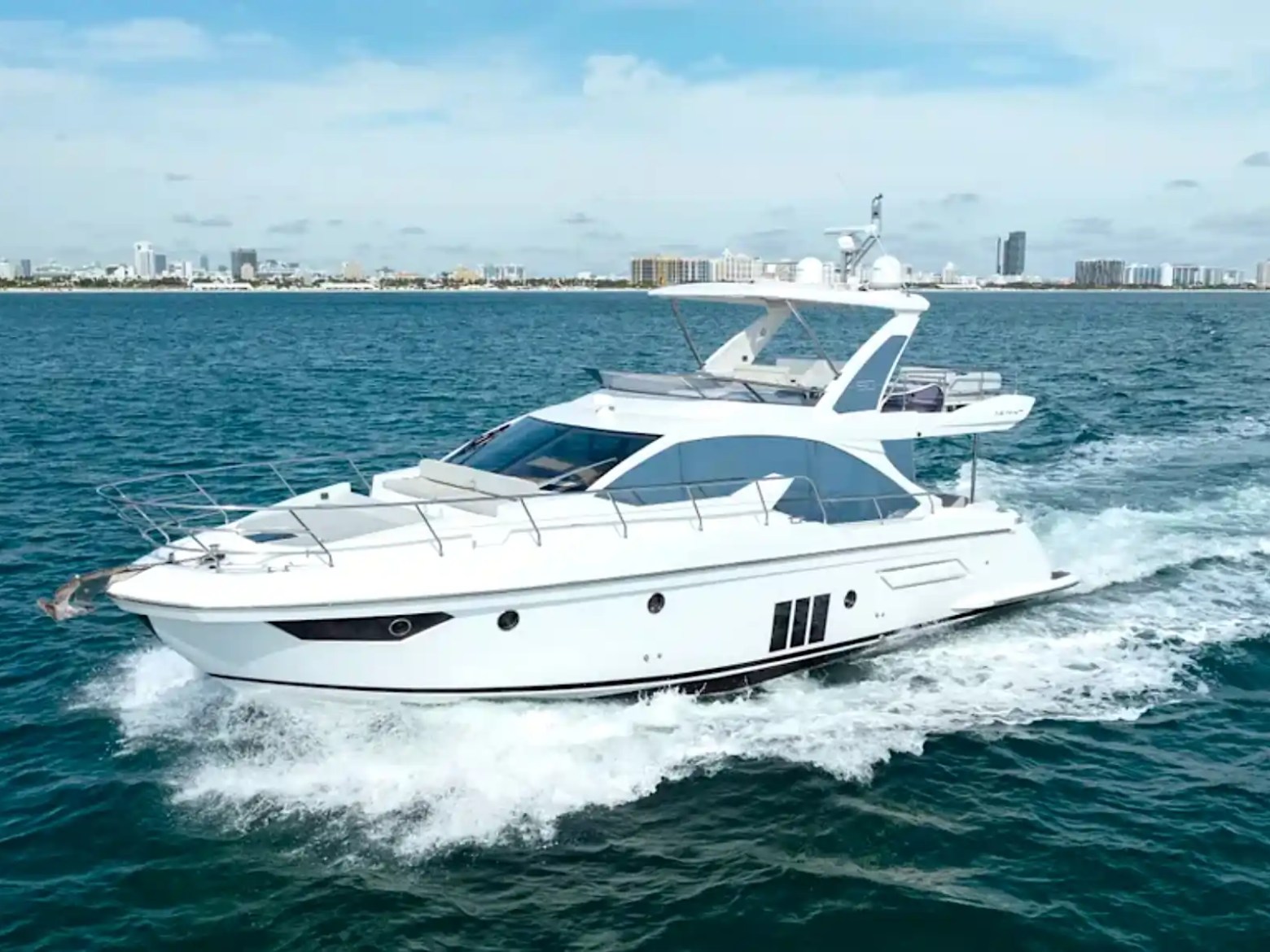 White yacht cruising on blue water with city skyline in the background.