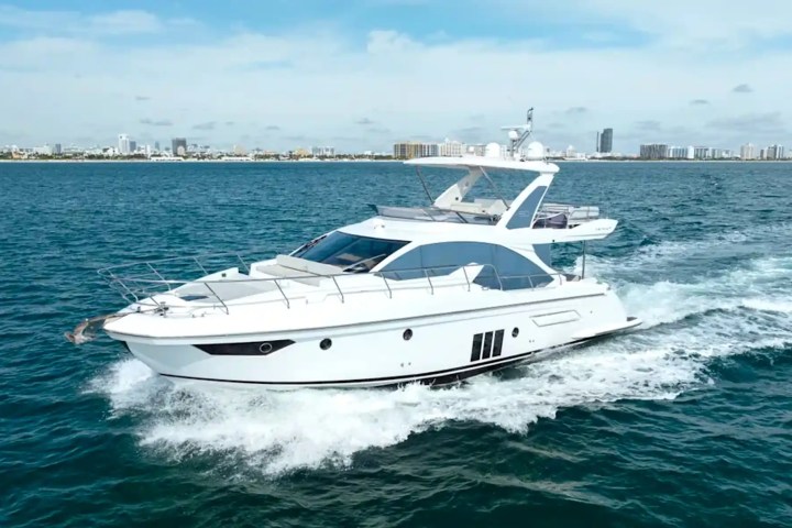 White yacht cruising on blue water with city skyline in the background.