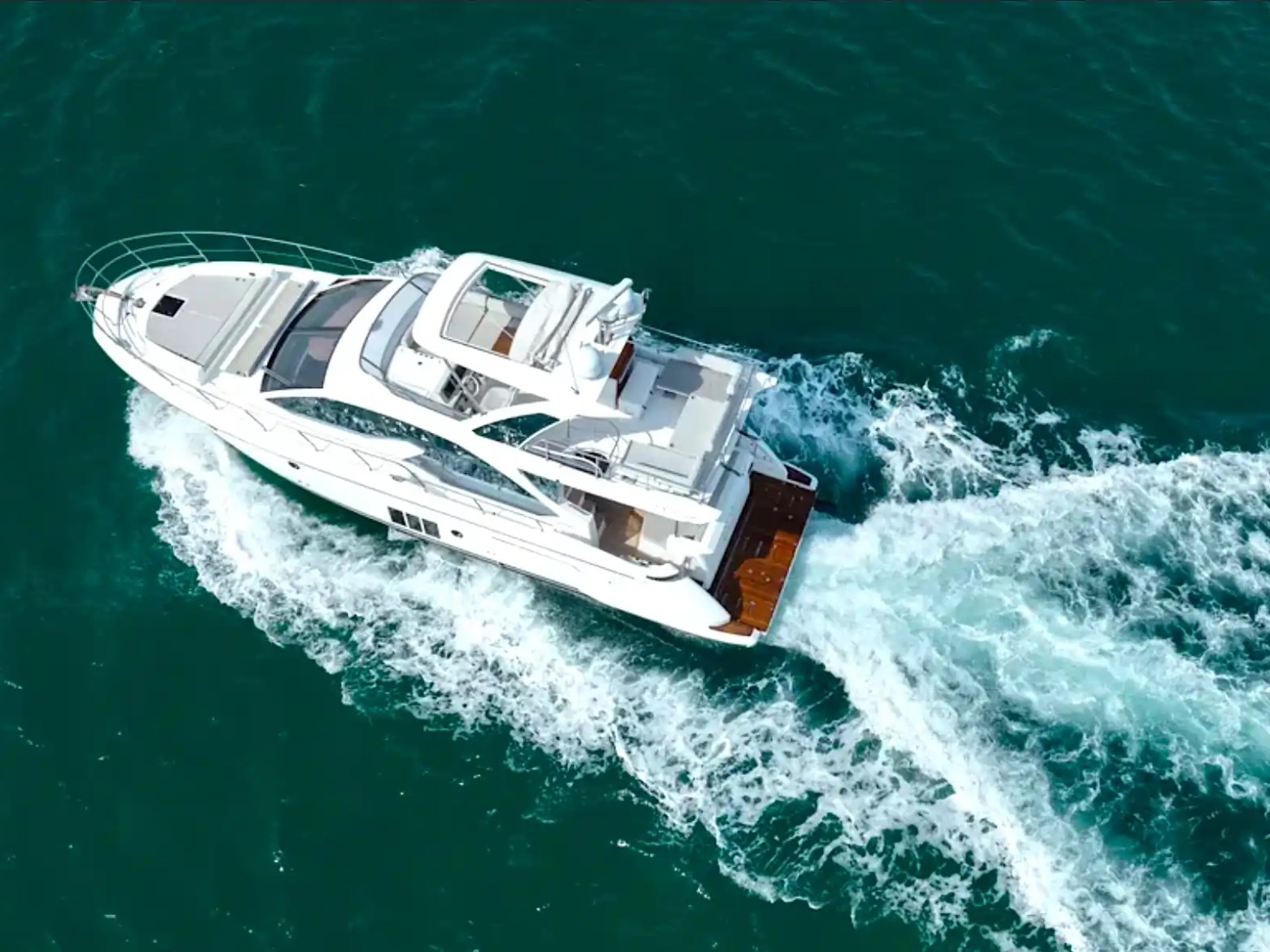 Aerial view of a white yacht cruising on open blue water, leaving a wake behind.