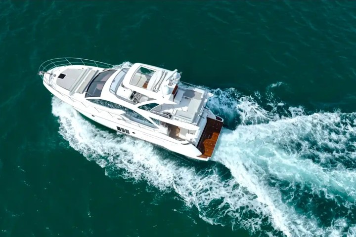 Aerial view of a white yacht cruising on open blue water, leaving a wake behind.