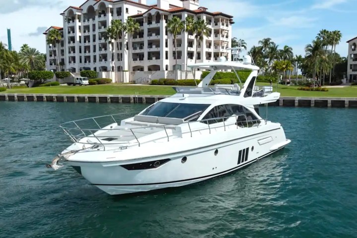 Luxurious white yacht on serene water near elegant waterfront buildings and palm trees.