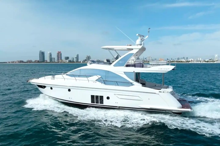 A white yacht cruising in clear blue water with a city skyline in the background.