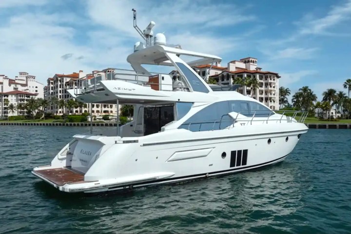 White luxury yacht sailing near waterfront condos and palm trees on a sunny day.