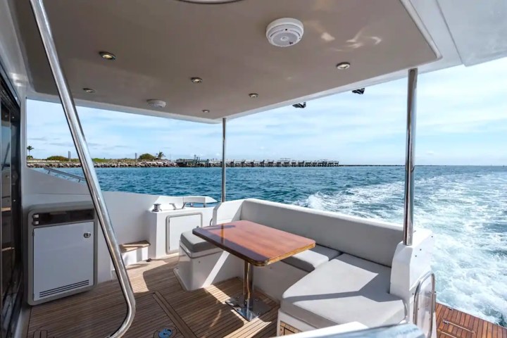 Boat deck with seating area and table, overlooking the ocean and distant coastline.