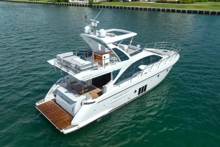Elegant white yacht on a calm blue waterway near a grassy shoreline.