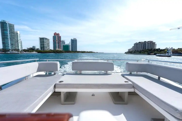 View from a boat deck with seating, water, and city skyline in the background.
